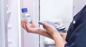 Gros plan sur les mains d'une biologiste utilisant un lecteur portable pour scanner le code-barres d'un flacon de culture cellulaire dans un réfrigérateur.